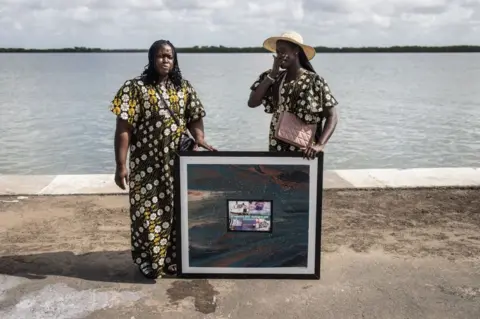 AFP Family members hold a painting in memory of their father during a ceremony for the anniversary of the capsizing of Le Joola in Ziguinchor on September 26, 2022. - September 26th, 2022 marks the 20th anniversary of the capsizing of Le Joola ferry between Dakar and Ziguinchor, known as the largest civil maritime disaster, 1,863 dead and missing according to the official report, more than 2,000 according to victim associations, of 12 different nationalities. Twenty years after Le Joola ferry sank, the Senegalese town where half of the nearly 1,900 dead lived will on Monday hold commemorations for a "wound that never heals".