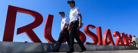 Getty Images Security personnel walk past a Russia 2018 sign near the Fisht Olympic Stadium in Sochi on June 12, 2018