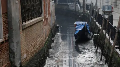 Reuters A gondola is pictured in a canal during a severe low tide in the lagoon city of Venice, Italy, February 17, 2023