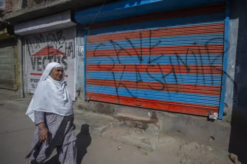 Abid Bhat A woman walks past a wall with graffiti on it, which reads: "Save Kashmir"