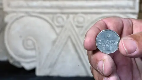 Yaniv Berman/Israel Antiquities Authority Five shekel coin against the background of the capital discovered