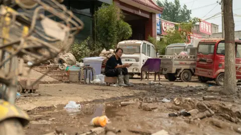 BBC/Joyce Liu Woman sits surrounded by flood debris