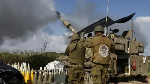 AFP An Israeli soldier wearing a patch on the back of his flack jacket showing Hezbollah leader Hassan Nasrallah as a target, stands in front of a self-propelled artillery howitzer in northern Israel as it fires a shell towards southern Lebanon (4 January 2023)