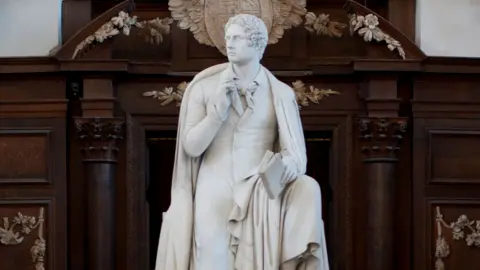Trinity College, University of Cambridge A statue of Lord Byron, holding a pencil to his chin, Wren Library, Trinity College