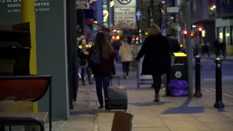 Young woman drags suitcase up street