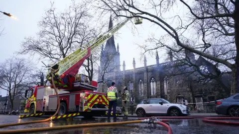 PA Media Daytime picture of firefighters using a crane to inspect the collapsed roof of the church.