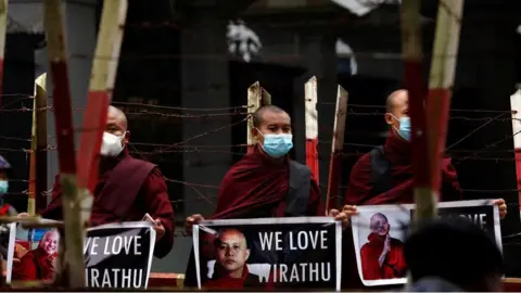 Getty Images Nationalist Buddhist monks hold posters with the image of detained monk Ashin Wirathu during a demonstration in front of a court house in Yangon on November 3, 2020.