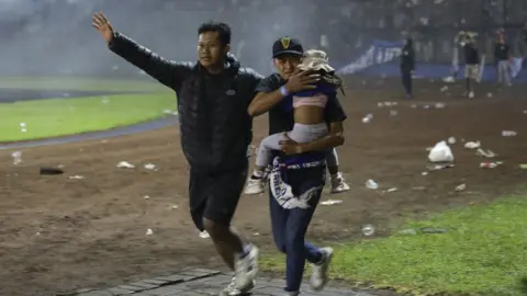 EPA Two men - with one carrying a child - run down the field to get away from the tear gas