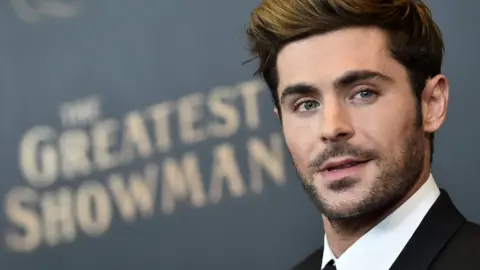 Getty Images Zac Efron looking wistful, with 'The Greatest Showman' written behind him.