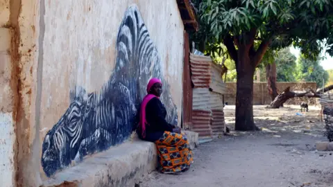 Clare Spencer Sarjo Beyai, a 20-year-old woman, says she sees tourists look at the side of her house but doesn’t speak English so can’t talk to them.