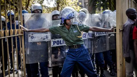 Getty Images Zimbabwean anti riot police officers close the gate of the Rainbow Towers where the election's results were announced, as supporters of the opposition party Movement for Democratic Change (MDC) protest against alleged widespread fraud in Harare, 1 August 2018