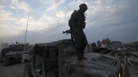 EFE/REX/Shutterstock An Israeli soldier standing on the hood of a military vehicle at a position in the Palestinian town of Beit Lahia, on the outskirts of Gaza City, northern Gaza Strip, 8 December 2023