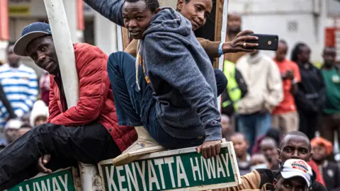 AFP People at a rally in Kenya - with some sitting on a signpost - 3 August 2022