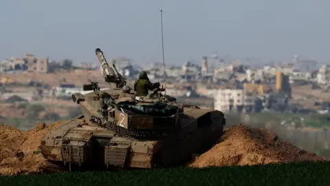 Reuters An Israeli tank manoeuvres along Israel's perimeter with northern Gaza, seen in the background (30 January 2024)