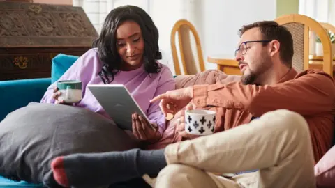 Getty Images Couple browse online while sitting on a sofa with drink