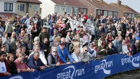 PA Media Crowd of people stand next to road