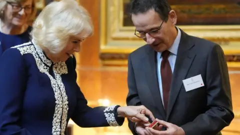 © His Majesty King Charles III 2024/PA Camilla looks at the tiny book she penned.