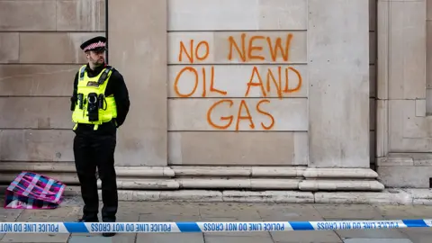 Getty Images A police officer stands outside graffiti that reads 'no new oil and gas' on the wall of the Bank of England in London