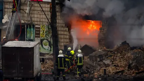 Getty Images Fire and rescue workers attend a building hit by a missile in central Kyiv