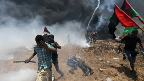 Reuters Palestinians run for cover during a protest near the Gaza-Israel border fence (14 May 2018)