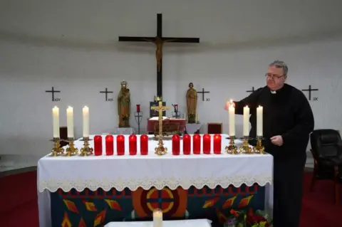 PA Media Father John Joe Duffy lights candles at St Michael's Church in Creeslough for the 10 victims