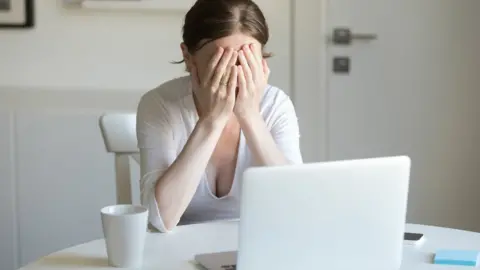 Getty Images Woman with her face in her hands in front of laptop