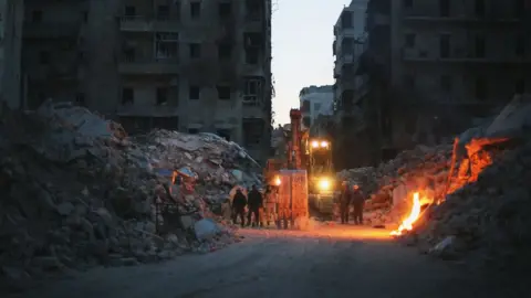  BBC/Larm Film/Aleppo Media Centre A digger lit up in the rubble in Aleppo