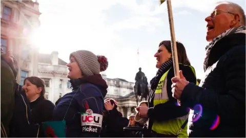 Getty Images UCU members in London hold signs and chant