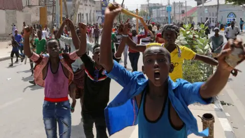 Reuters boys running towards camera, gesturing, one holding a stone in his hand
