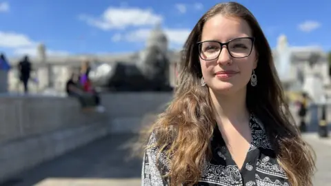 BBC News Rebecca, 21, smiles at the camera in London's Trafalgar Square