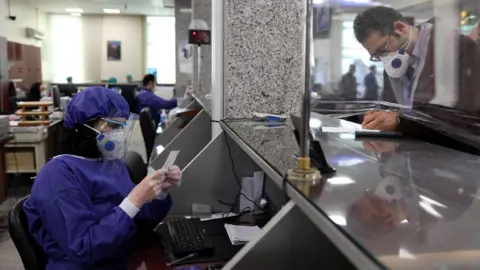 Reuters A bank employee wear protective masks in Tehran, Iran (17 March 2020)