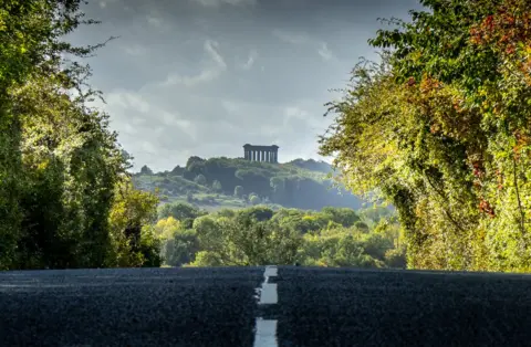 Darren Cheverton A road between trees with a columned monument on a hill in the background