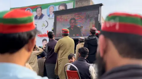 People at a rally for Atif Khan in Khyber Pakhtunkhwa watch him speak on a big screen on the back of a truck 3 Feb 2024
