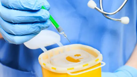 Getty Images Gloved hand binning a syringe