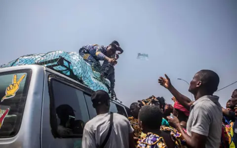 Getty Images A man, standing on top of a car, throws a bottle of water to another man
