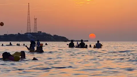 People bathe in the Mediterranean sea water off a beach in Libya's capital Tripoli near sunset on August 18, 2020.