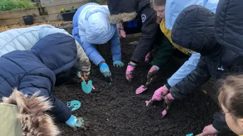 John Devine/BBC Children gardening in a muddy raised bed