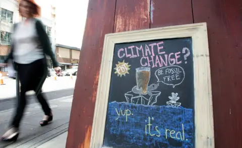 Getty Images A woman walks by a sign about climate change in front of a bar in downtown San Francisco. September 2018