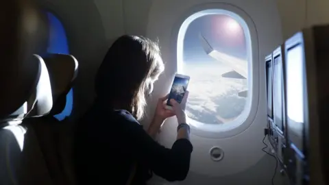 Getty Images A woman takes a picture out of a plane window