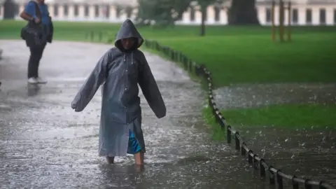 PA Media A woman wades through a flooded path in St James's Park in central London