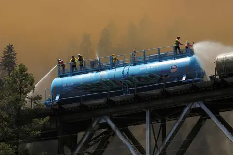 David Swanson / Reuters Firefighters spray water from a fire train over Rock Creek Bridge as a fire grows in Plumas National Forest, California