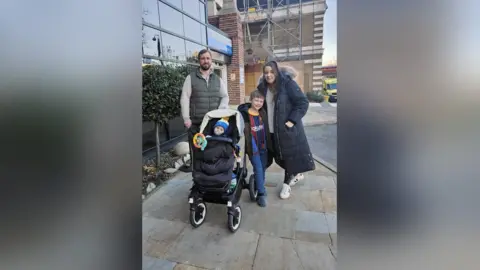 PA Media Teddy with his mum, Emma and dad Greg and older brother Theo