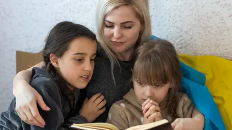 Getty Images Mother and daughter reading a book with a flag of Ukraine on a bed, stock photo