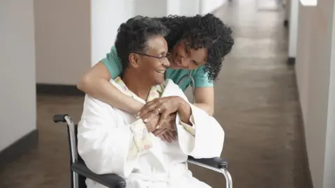 Getty Images Elderly woman and health professional. Both smiling.