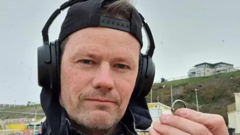 Aaron Le Arm Man with headphones holding a ring