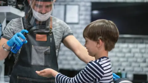 Getty Images A hairdresser spraying sterilising fluid onto a boy's hands