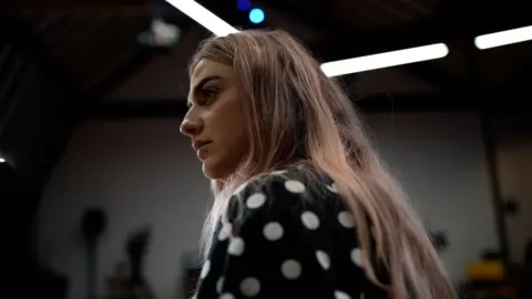 Side-profile still of Roxanne listening to other women speak