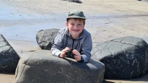 Dale Greetham Rylie crouches between rocks with a pair of binoculars