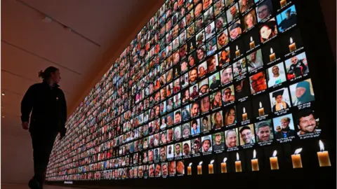 AFP A visitor looks at a giant backlight screen bearing the portraits of the Israeli people who were killed during the October 7 attacks by Hamas in southern Israel or those who died during the ongoing battles between Israel and the Palestinian militant group Hamas in Gaza, at the National Library in Jerusalem, on January 25, 2024