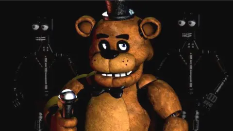 Scottgames Freddy - the large animatronic bear and main enemy of the series - holds a microphone and glares into the camera. On either side of him in the dark background, two robot skeletons with big, cartoon eyes are visible.